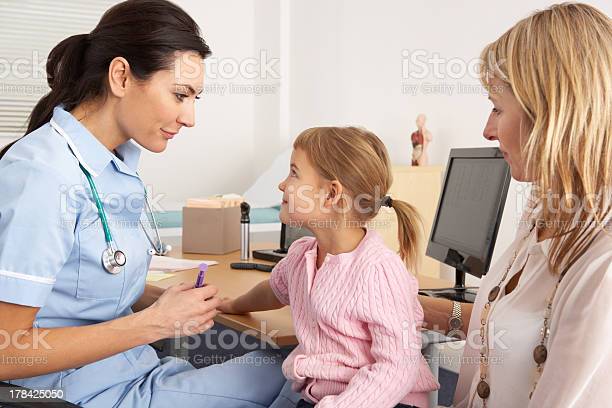 British nurse about to inject young child in consultation room looking at each other