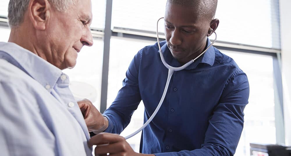 Doctor Listening To Chest Of Senior Male Patient During Medical Exam In Office