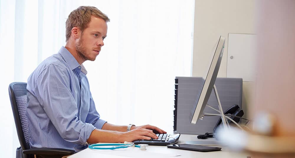 Male Doctor In Office Working At Computer