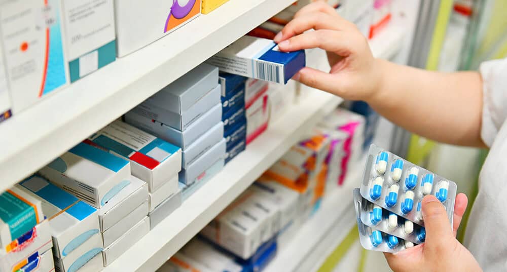 Pharmacist holding medicine box and capsule pack in pharmacy drugstore.