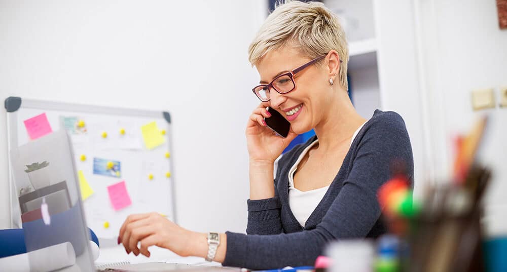 Blonde woman sitting at a desk, she is on her mobile phone